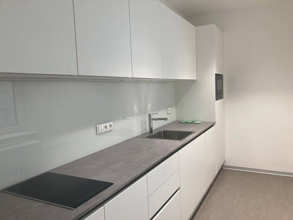 Moderne Küchenzeile mit weißen Schränken, grauer Arbeitsplatte und integriertem Kochfeld und Spüle.