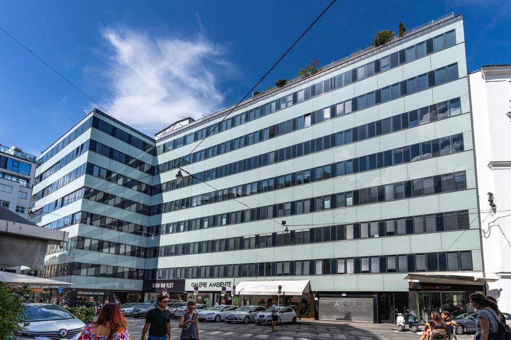 Großes Bürogebäude mit mehreren Etagen und Geschäften im Erdgeschoss in einer belebten Stadtansicht.