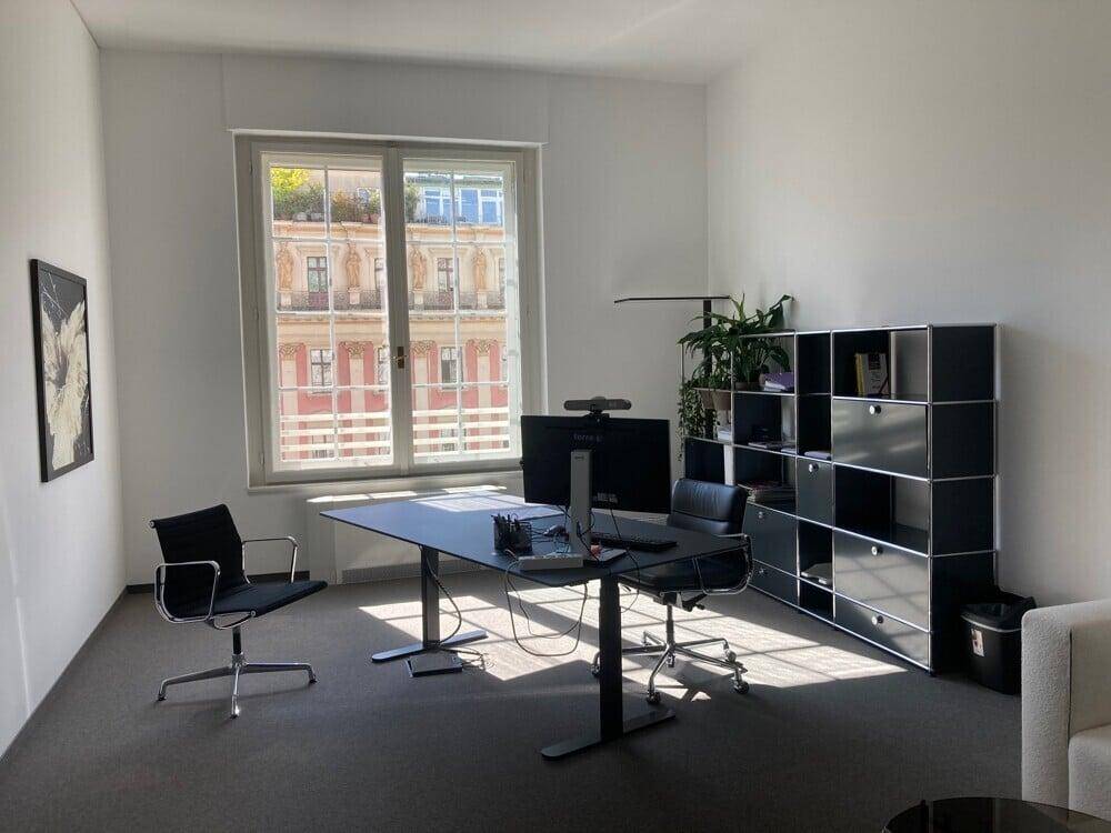 Modernes Büro mit Teppichboden, großem Fenster und ergonomischem Schreibtisch.