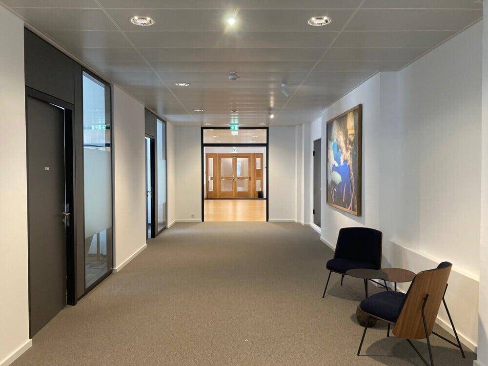 Langer Bürogang mit Teppichboden, modernen Türen und Kunstwerken an den Wänden.
