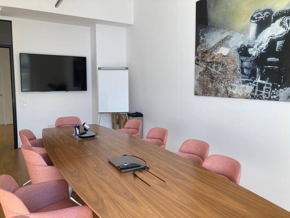 Moderner Konferenzraum mit großem Holztisch, bequemen Stühlen und Wandfernseher.
