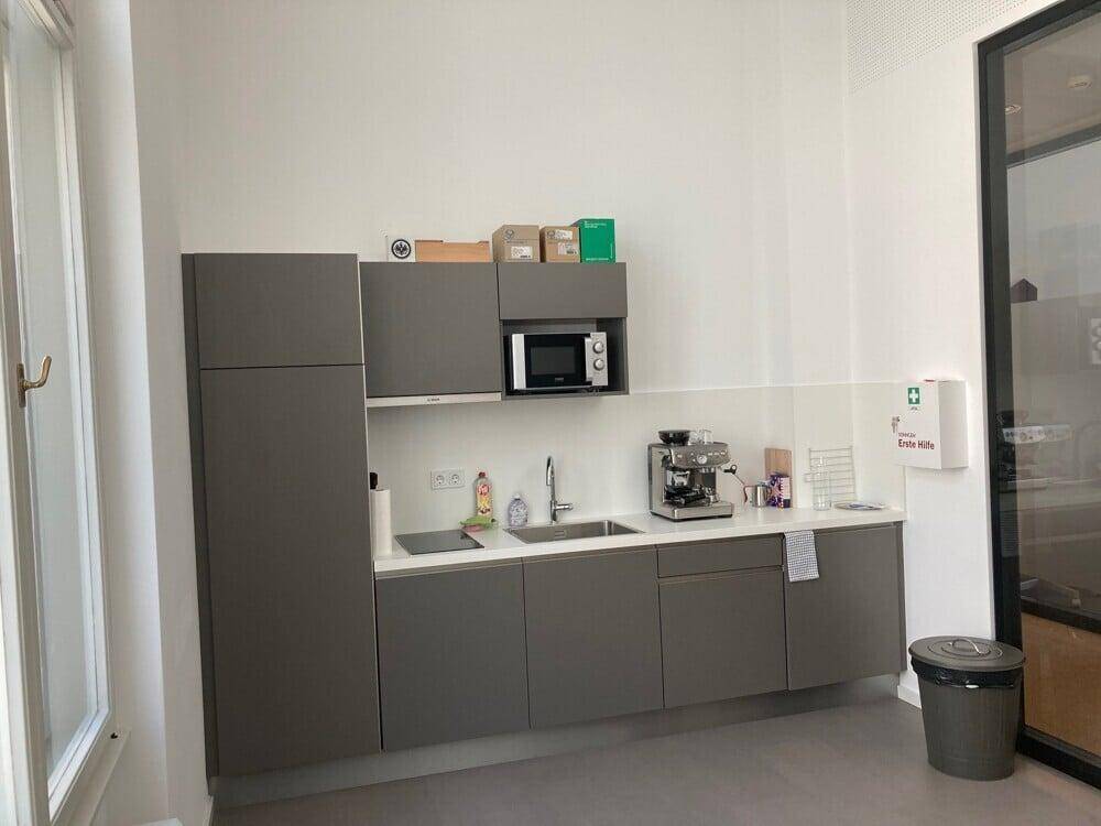 Kleine, moderne Teeküche mit grauen Schränken, Mikrowelle und Kaffeemaschine.