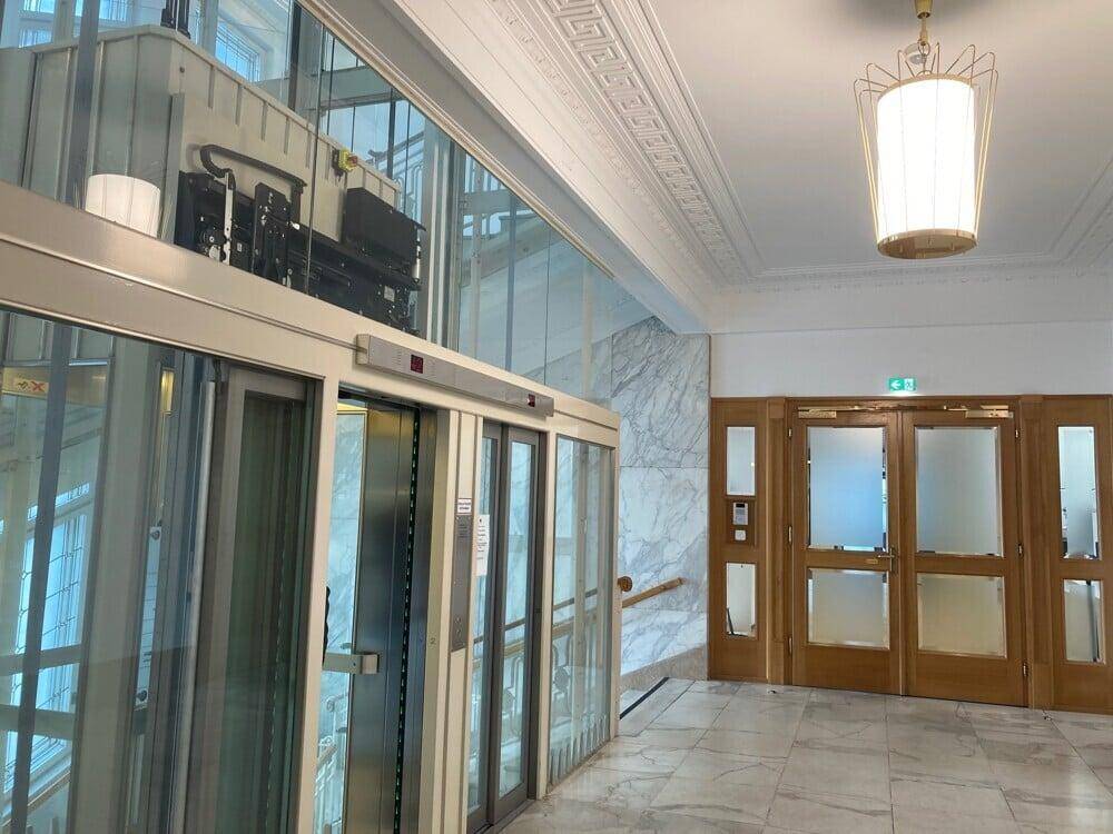 Heller Eingangsbereich mit Marmorboden, Holztüren und einem modernen Glasaufzug.