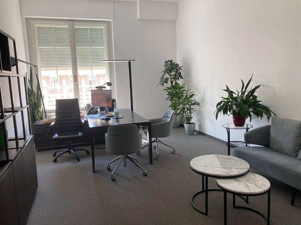 Geräumiges Büro mit Teppichboden, Sitzbereich und Blick auf die Stadt durch das Fenster.