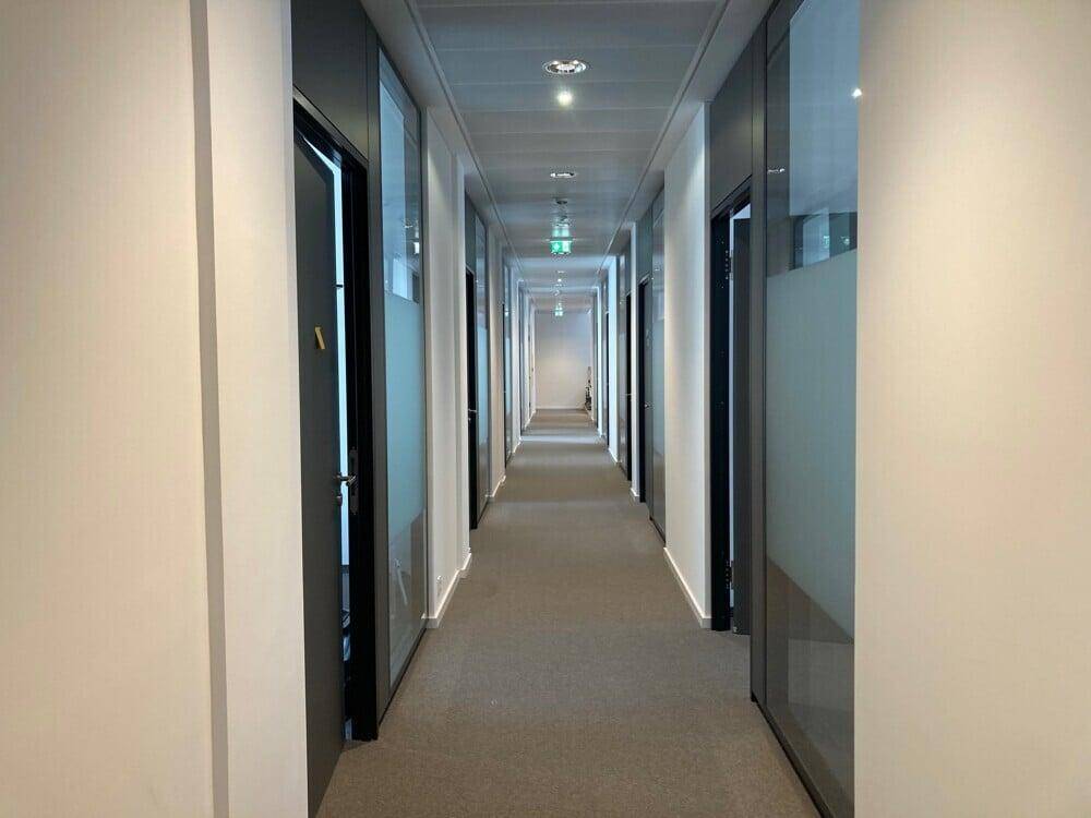 Langer, moderner Bürogang mit Teppichboden und vielen Türen zu einzelnen Büros.