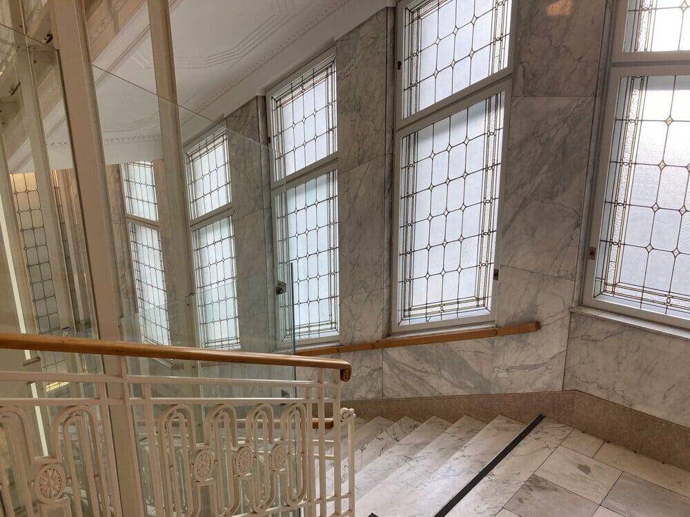 Elegantes Treppenhaus mit Marmorverkleidung, verzierten Fenstern und einem modernen Aufzug.