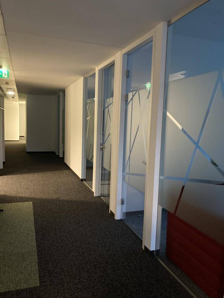 Heller Bürogang mit Teppichboden und modernen Glastüren zu den einzelnen Büroräumen.