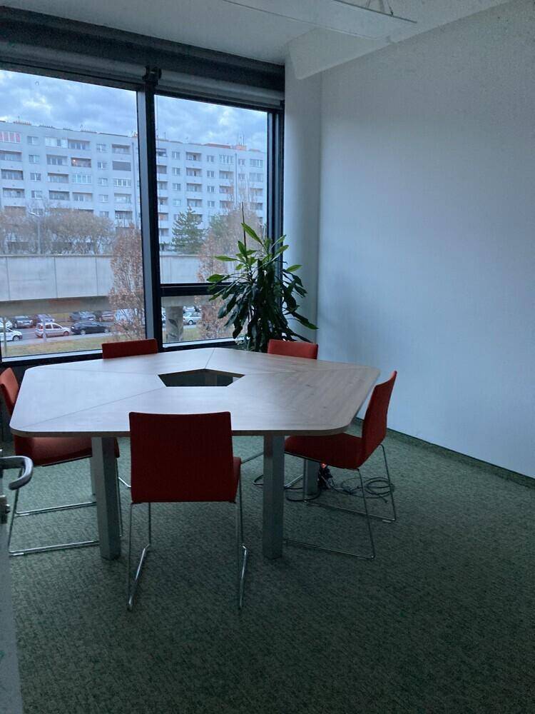 Kleiner Besprechungsraum mit achteckigem Tisch, roten Stühlen und Blick nach draußen.