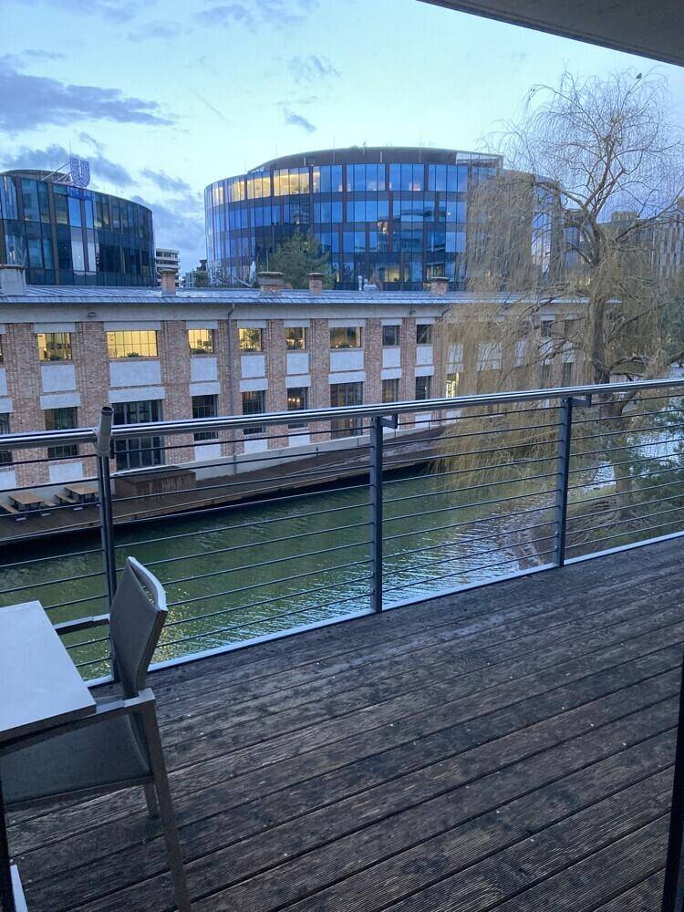 Balkon mit Holzboden und Geländer, bietet einen schönen Blick auf das Wasser und umliegende Gebäude.