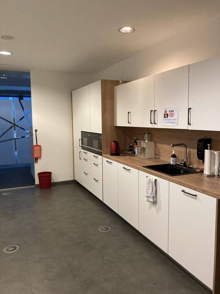 Moderne Büroküche mit weißen Schränken, Holzarbeitsplatte und integrierten Geräten.