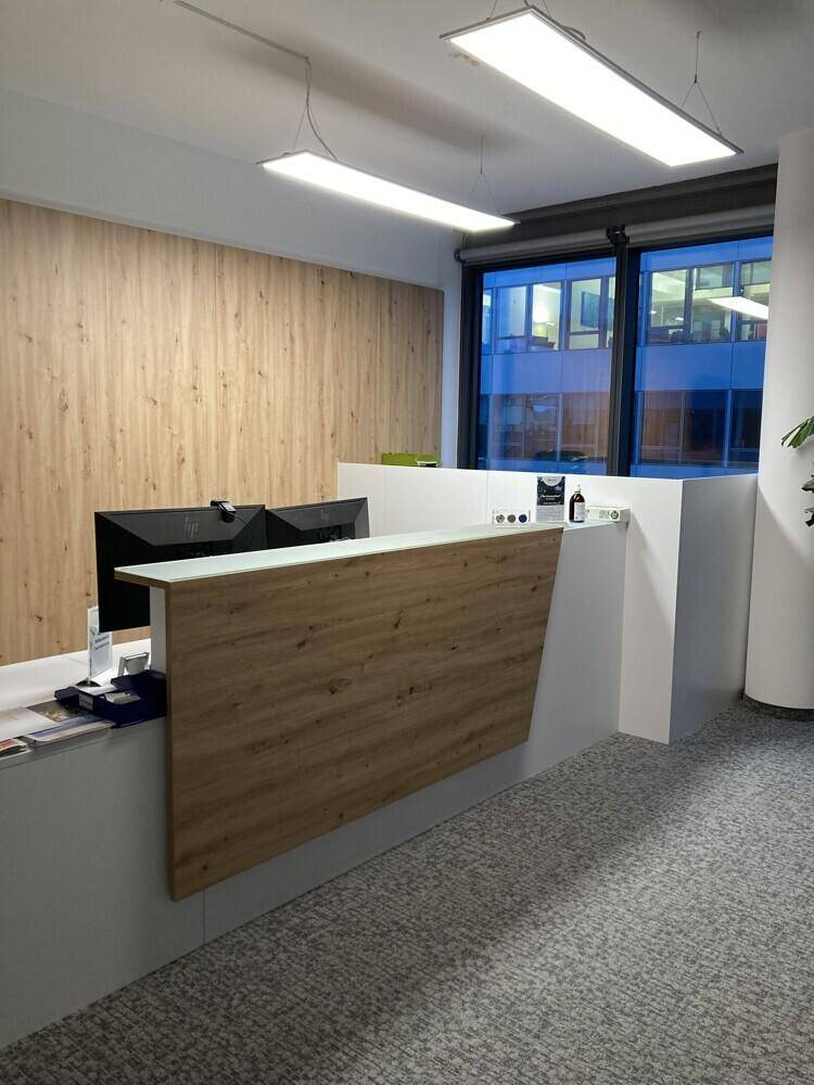 Moderner Empfangsbereich mit Holzverkleidung, weißer Theke und Teppichboden.