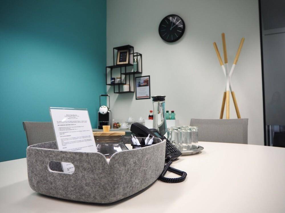 Kleiner Besprechungsbereich mit Kaffeemaschine, Telefon und modernem Design mit türkiser Akzentwand.