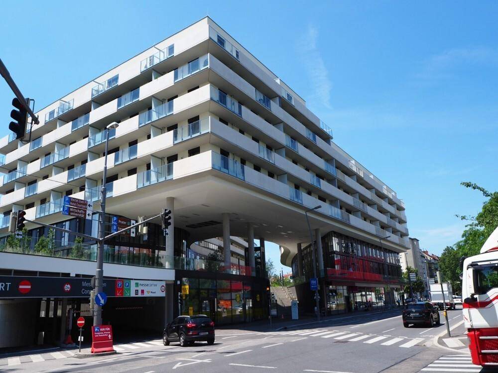 Modernes Wohngebäude mit vielen Balkonen und Geschäften im Erdgeschoss an einer belebten Straße.
