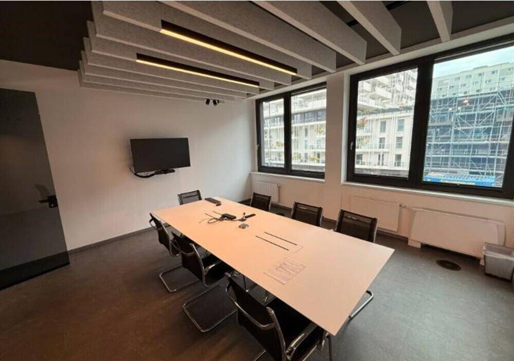 Heller Konferenzraum mit großem Tisch, bequemen Stühlen und Wandfernseher für produktive Meetings.