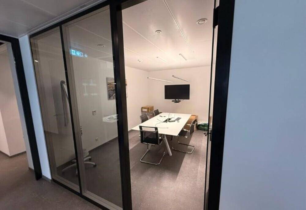 Besprechungsraum mit Glastür, Wandfernseher und modernem Konferenztisch, ideal für Präsentationen.