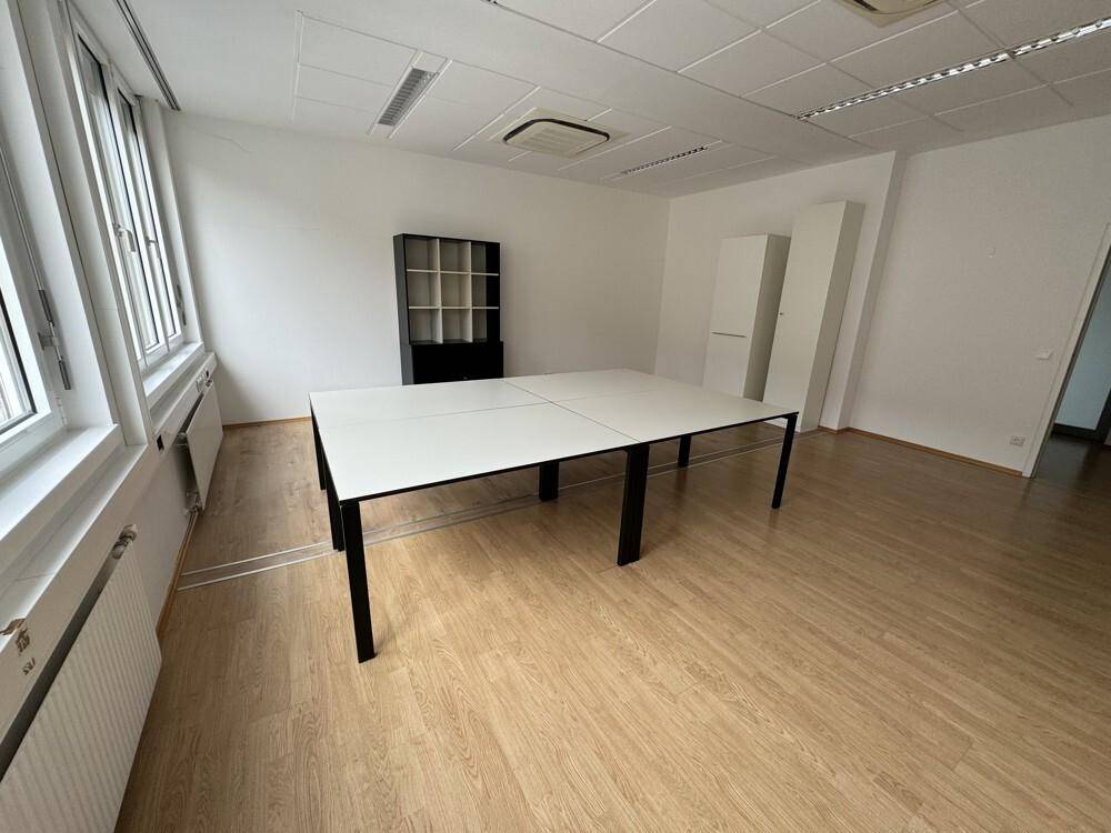 Helles Büro mit Holzboden, großem weißen Tisch und Schränken, bereit zur Nutzung.