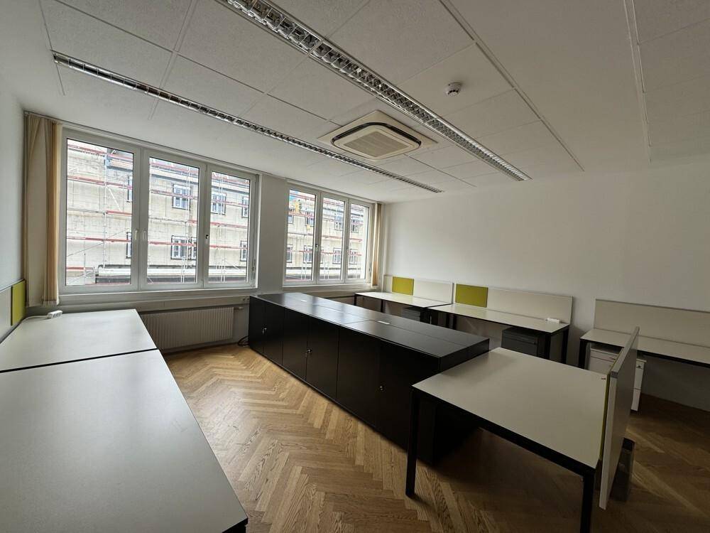 Geräumiges Büro mit Fischgrätparkett, mehreren Schreibtischen und großen Fenstern.