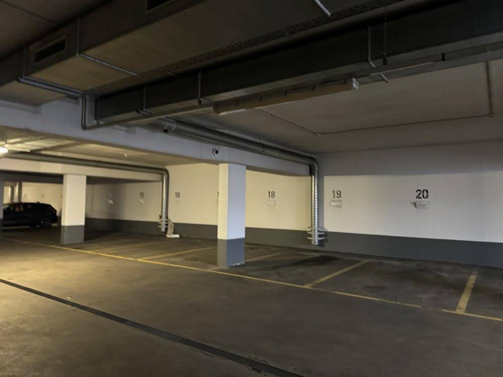 Tiefgarage mit nummerierten Stellplätzen, Betonpfeilern und sichtbaren Lüftungsrohren.