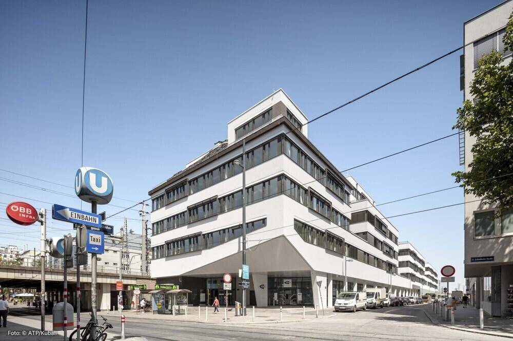 Weißes Bürogebäude mit moderner Fassade und vielen Fenstern an einer Kreuzung mit U-Bahn-Station.