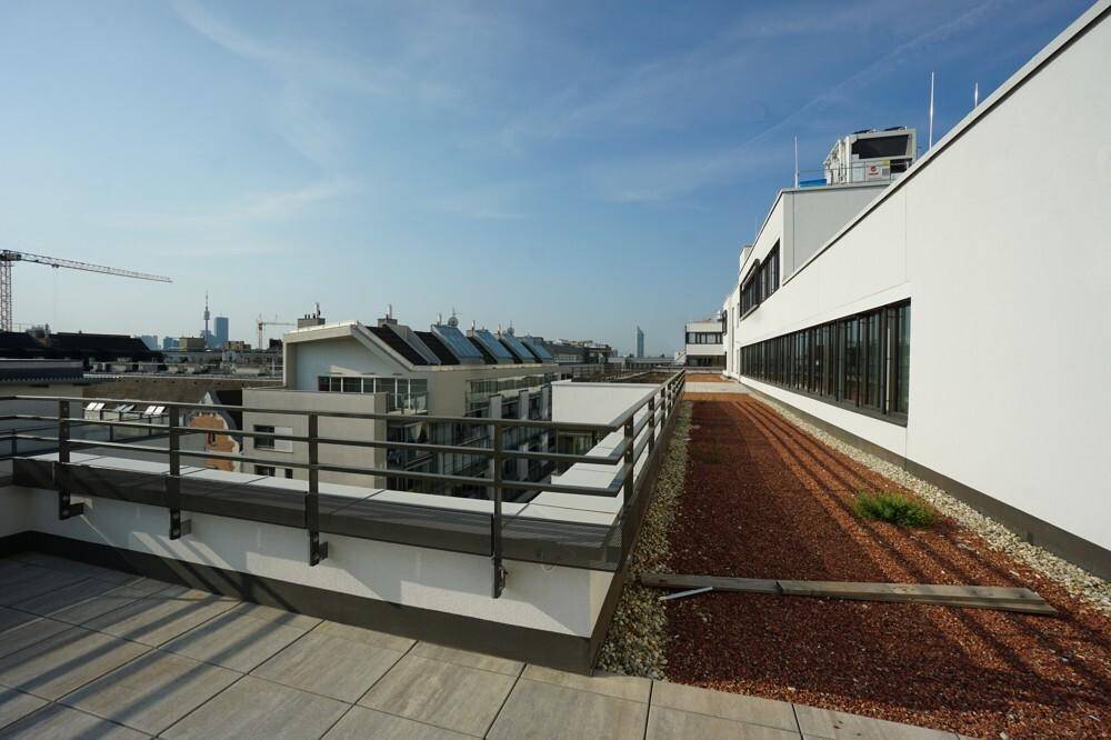 Geräumige Dachterrasse mit Steinplatten und Kiesflächen, umgeben von einem Geländer mit Stadtblick.