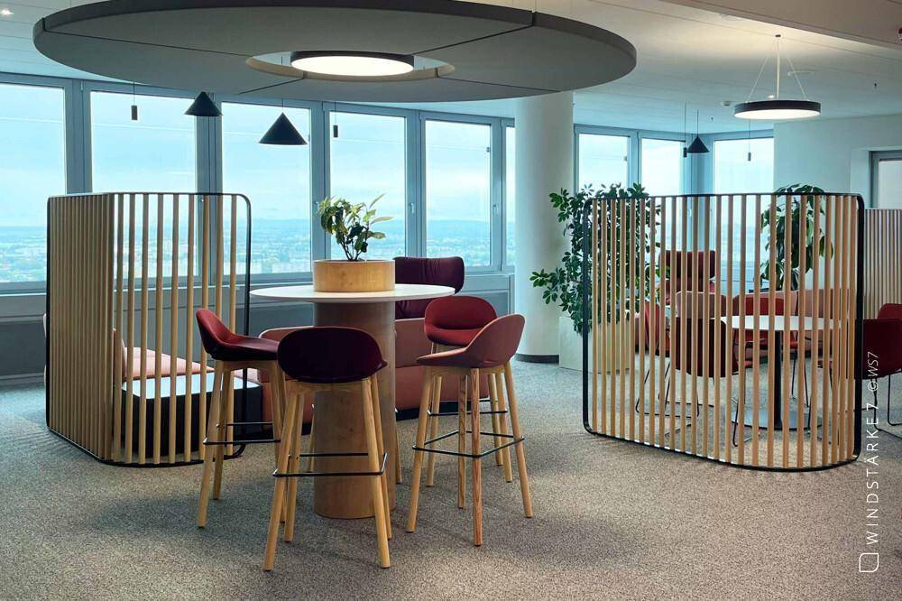 Moderner Loungebereich mit runden Tischen, Barhockern und dekorativen Holzlamellen als Raumteiler.