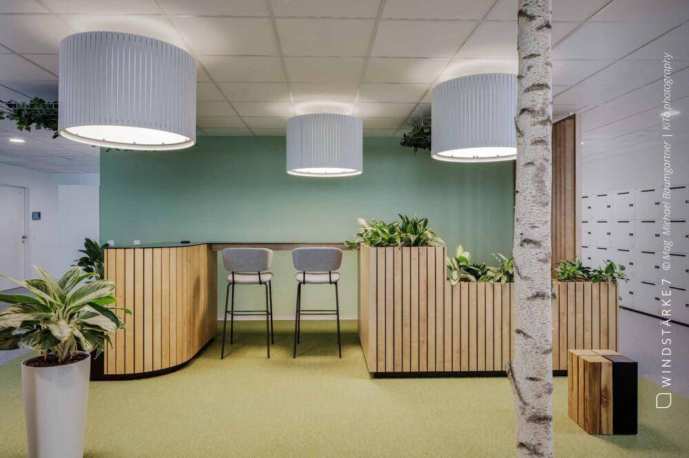 Kreativer Loungebereich mit Holzelementen, Pflanzen und großen zylindrischen Deckenleuchten.