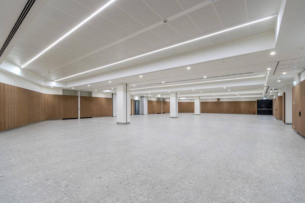 Großer, leerer Saal mit hohen Decken, Säulen und Holzverkleidungen an den Wänden.