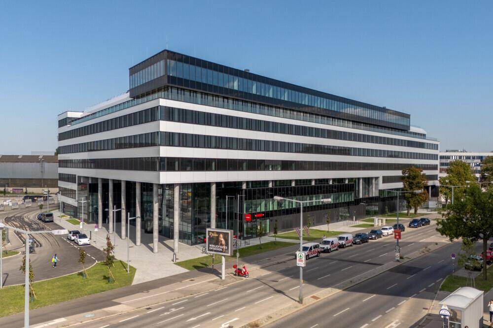 Modernes Bürogebäude mit markanter Architektur, Glasfassade und umliegender Infrastruktur an einem sonnigen Tag.