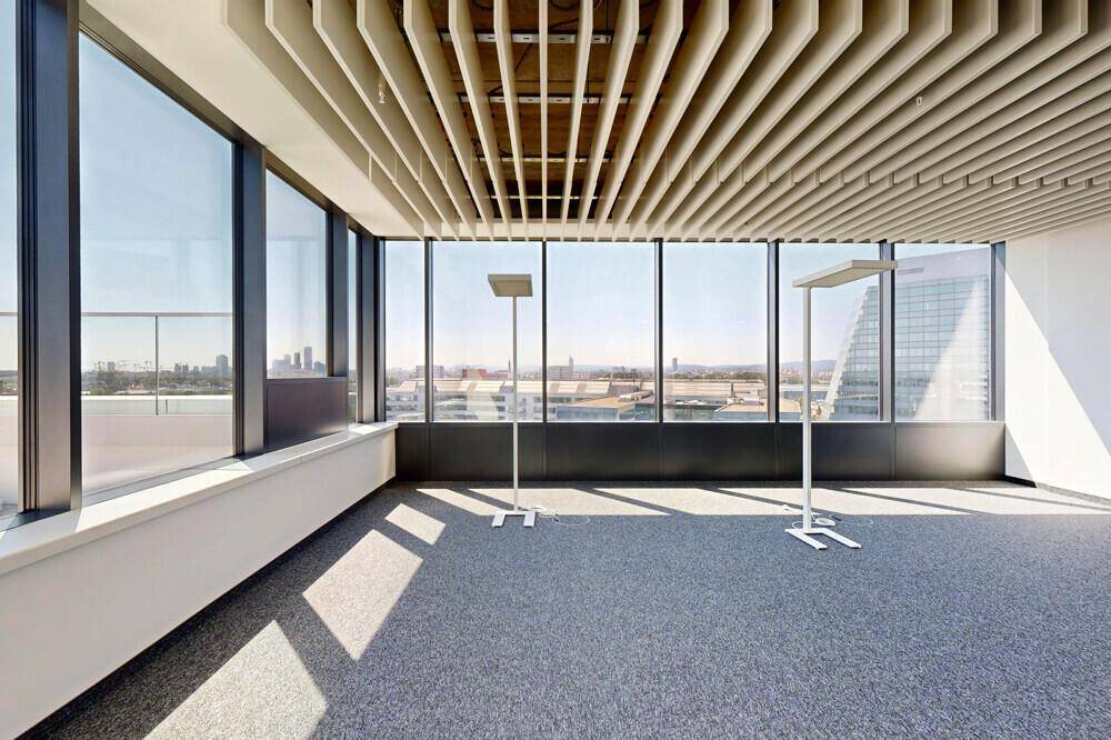 Helles Büro mit großen Fenstern, die einen weiten Blick über die Stadt bieten, und einer modernen Deckenkonstruktion.