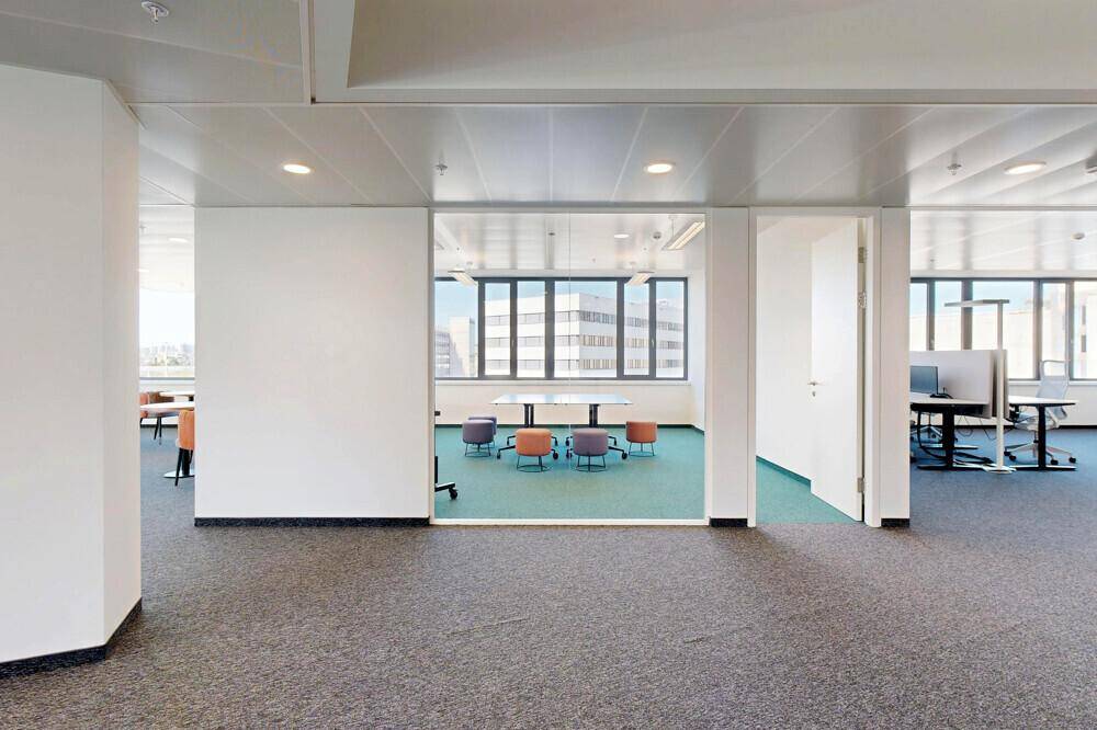 Offener Bürobereich mit verschiedenen Arbeitszonen, Teppichboden und Blick in angrenzende Räume.