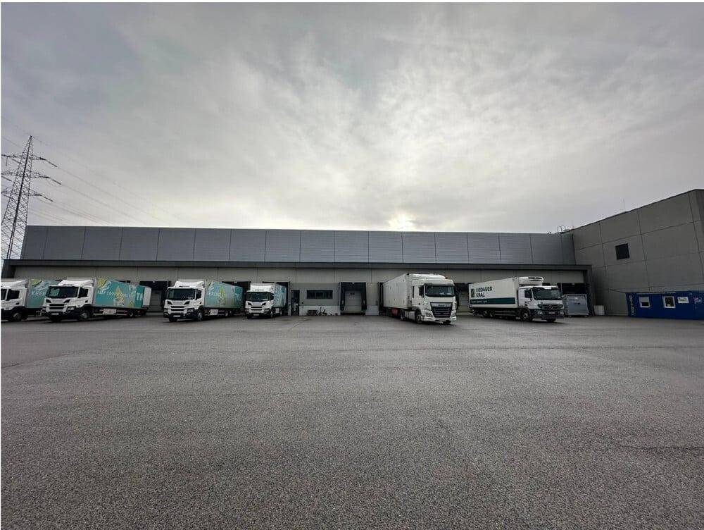 Eine weitere Außenansicht des Logistikzentrums mit zahlreichen Lastwagen an den Laderampen und einem großen Vorplatz.