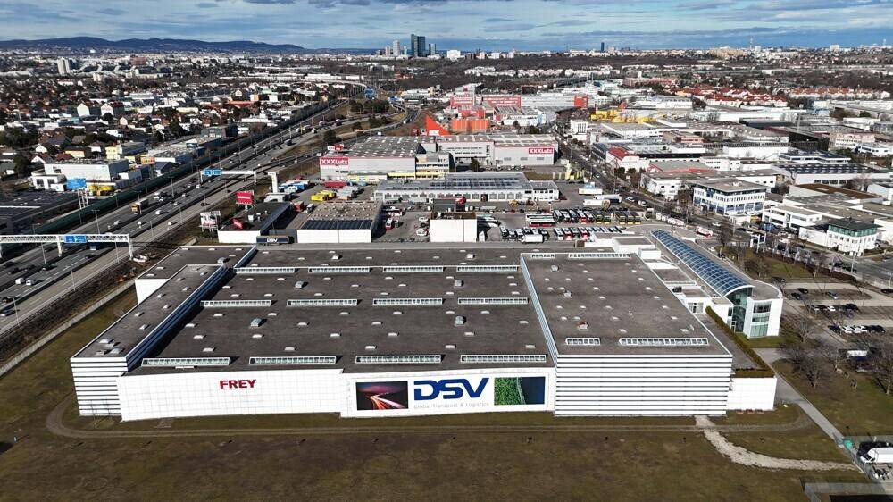 Weitläufige Ansicht des Logistikgebäudes mit Firmenlogos an der Fassade und großem Parkplatzbereich.