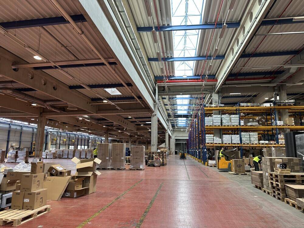 Weitläufiger Lagerraum mit hohen Decken, Oberlichtern und einigen Waren auf Paletten.