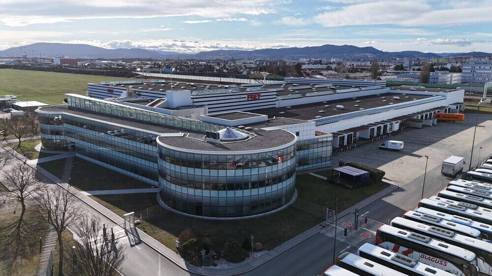 Luftaufnahme des modernen Logistikzentrums mit Bürogebäude, Glasfassade und großem Busparkplatz.