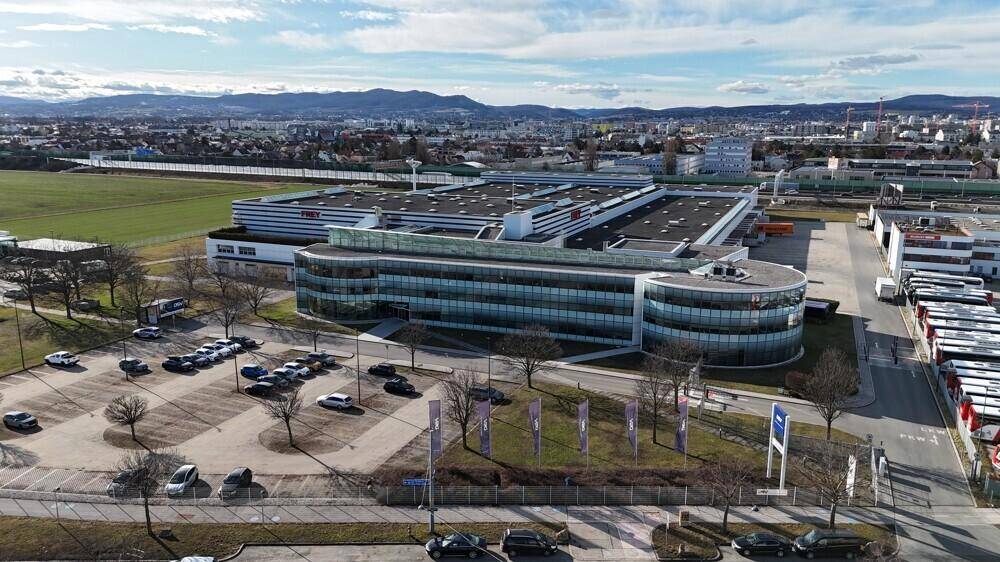 Übersicht des modernen Bürogebäudes mit geschwungener Glasfassade und angrenzendem Parkplatz.