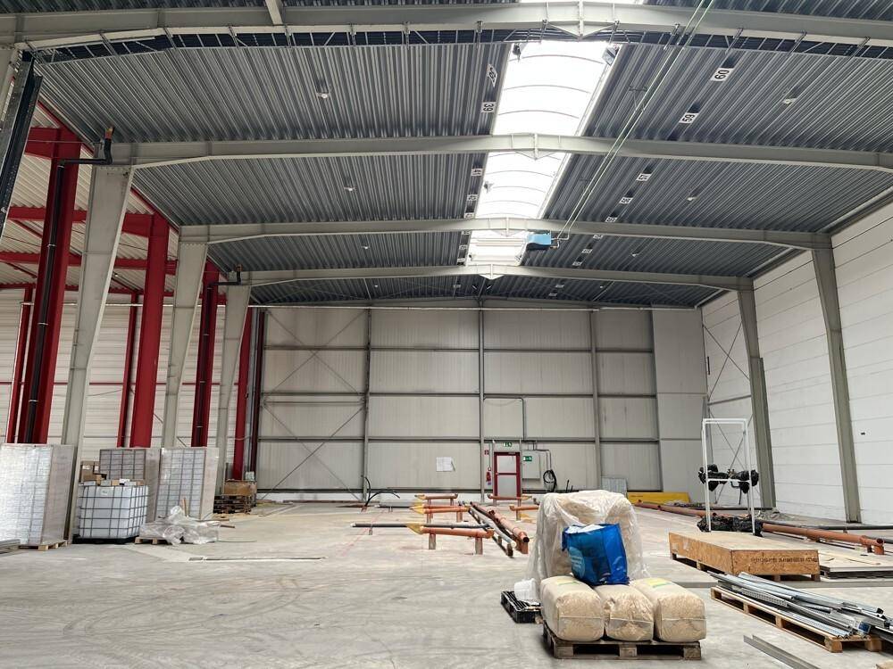 Weitläufige, leere Industriehalle mit hohen Decken, sichtbaren Trägern und einigen Baumaterialien am Boden.