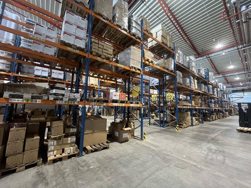 Lagerhalle mit hohen Regalsystemen, gefüllt mit Waren und Kartons auf Paletten, bereit zur Lagerung.