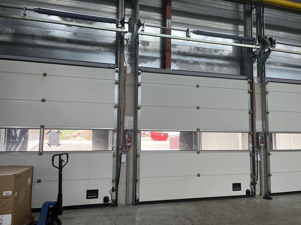 Innenansicht von mehreren großen, weißen Industrietoren mit Fenstern und einem Hubwagen im Vordergrund.