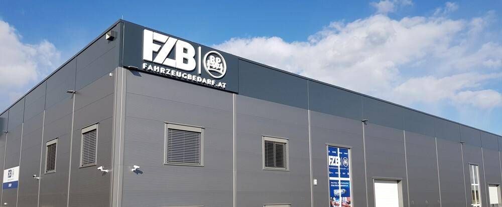 Ansicht der modernen Gebäudefassade mit großem Firmenlogo und Rollläden an den Fenstern unter blauem Himmel.