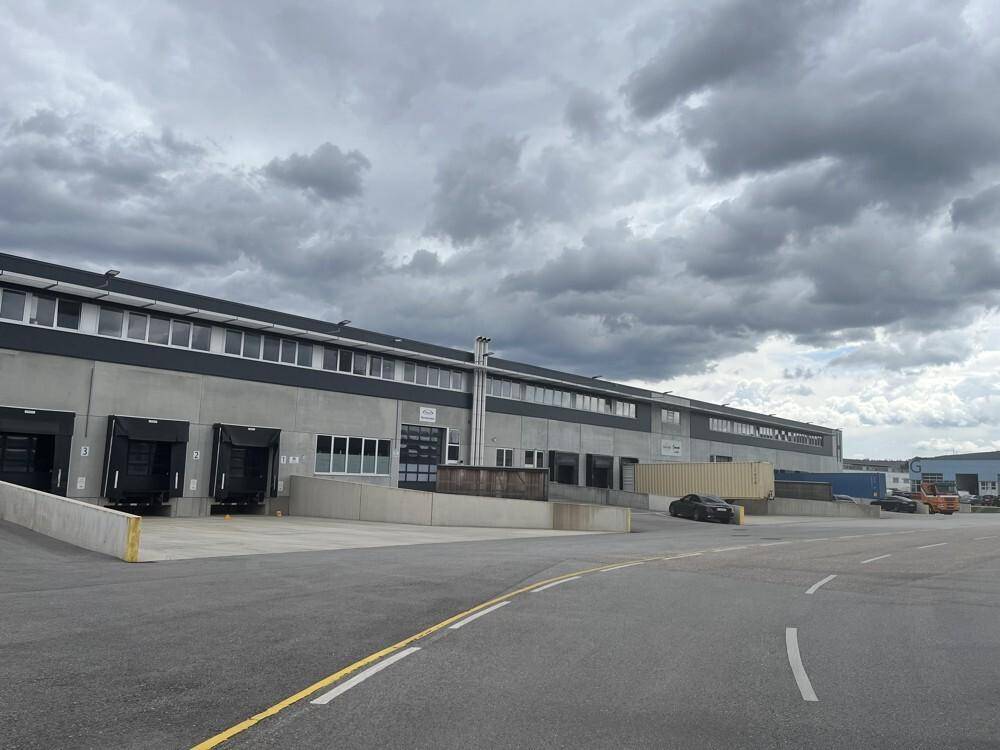 Weitläufiges Industriegebäude mit mehreren Laderampen und einer großen asphaltierten Zufahrt unter bewölktem Himmel.