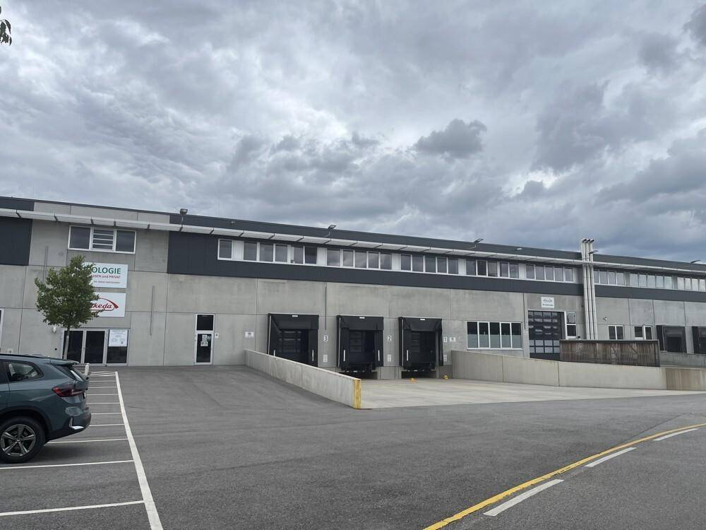 Modernes Industriegebäude mit Laderampen und einem großen Parkplatz für Fahrzeuge unter bewölktem Himmel.