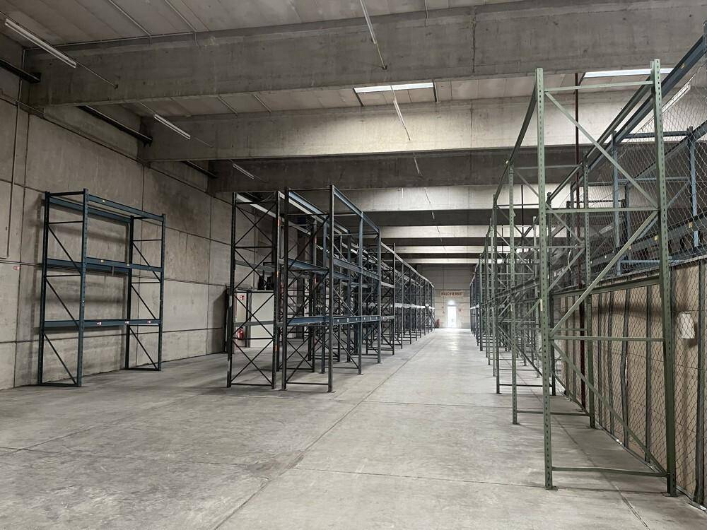 Lagerhalle mit Betonboden, hohen Decken und Reihen von Metallregalen für die Lagerung.