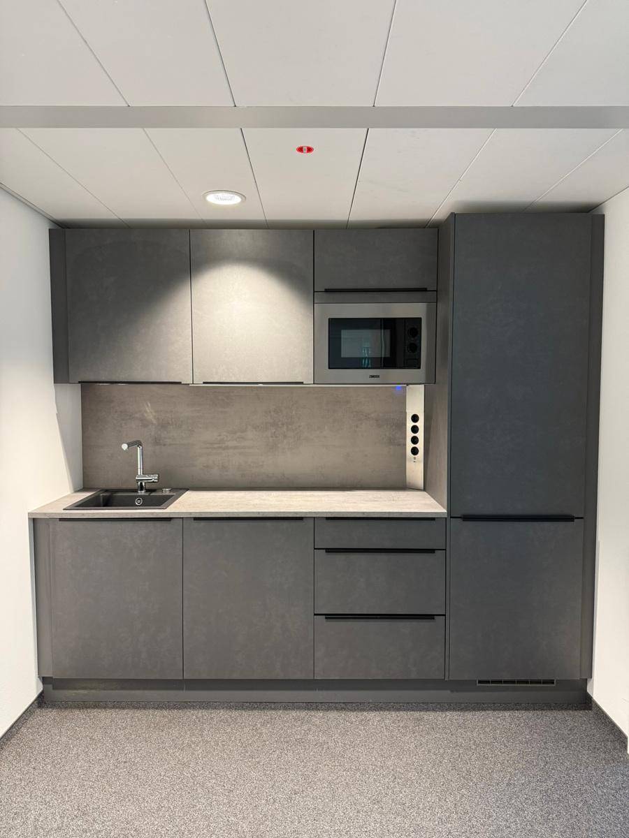 Moderne graue Küchenzeile mit integriertem Kühlschrank, Mikrowelle und Spülbecken.