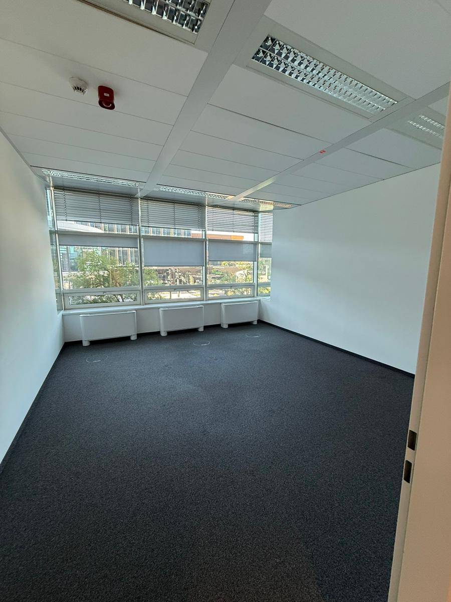 Helles Büro mit Teppichboden und Fenstern, die mit horizontalen Jalousien für Sonnenschutz ausgestattet sind.