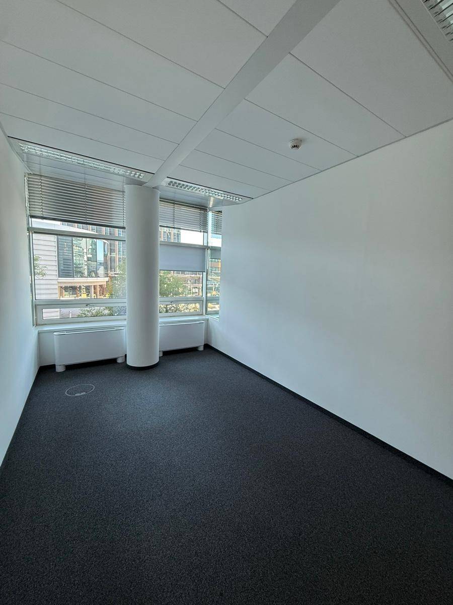 Eckbüro mit Teppichboden und Fenstern, die mit Jalousien und einer Säule im Raum versehen sind.