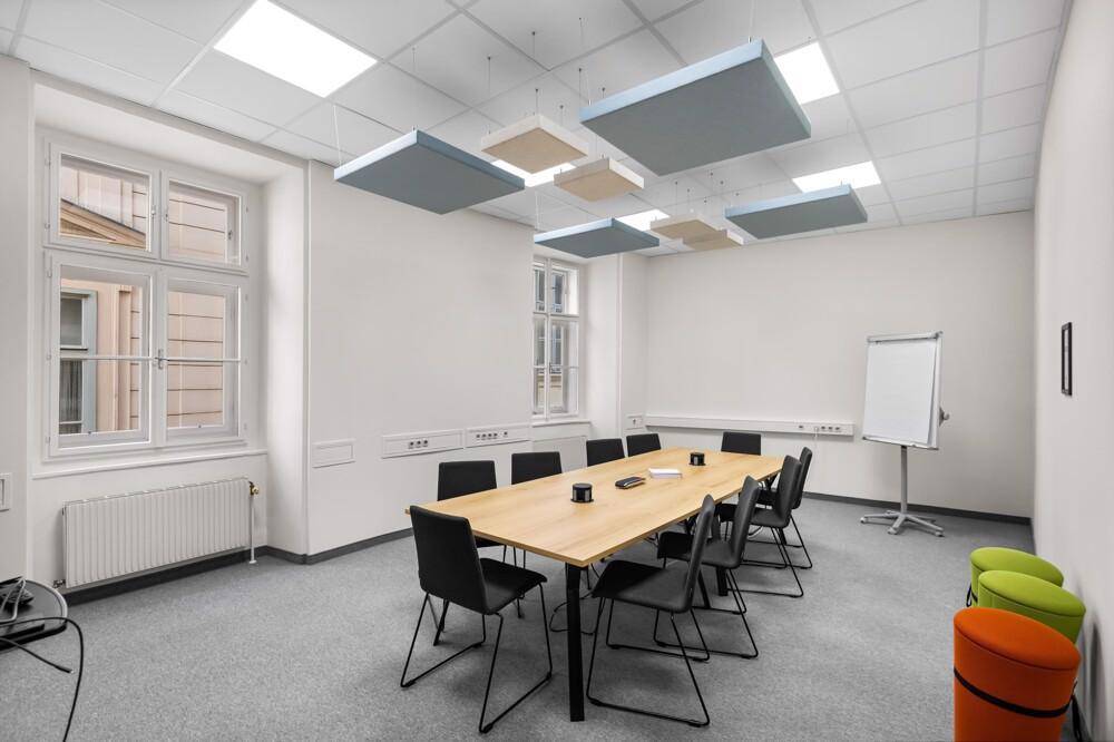 Konferenzraum mit großem Holztisch, bequemen Stühlen und schallabsorbierenden Deckenpaneelen für Besprechungen.