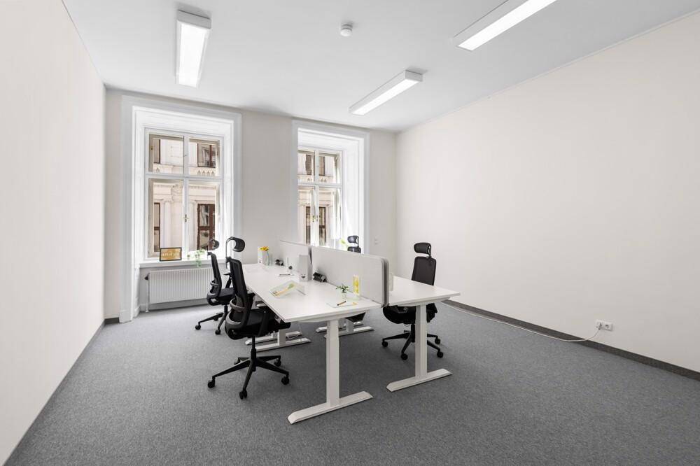Helles Büro mit mehreren modernen Arbeitsplätzen, grauem Teppichboden und großen Fenstern zur Straße.