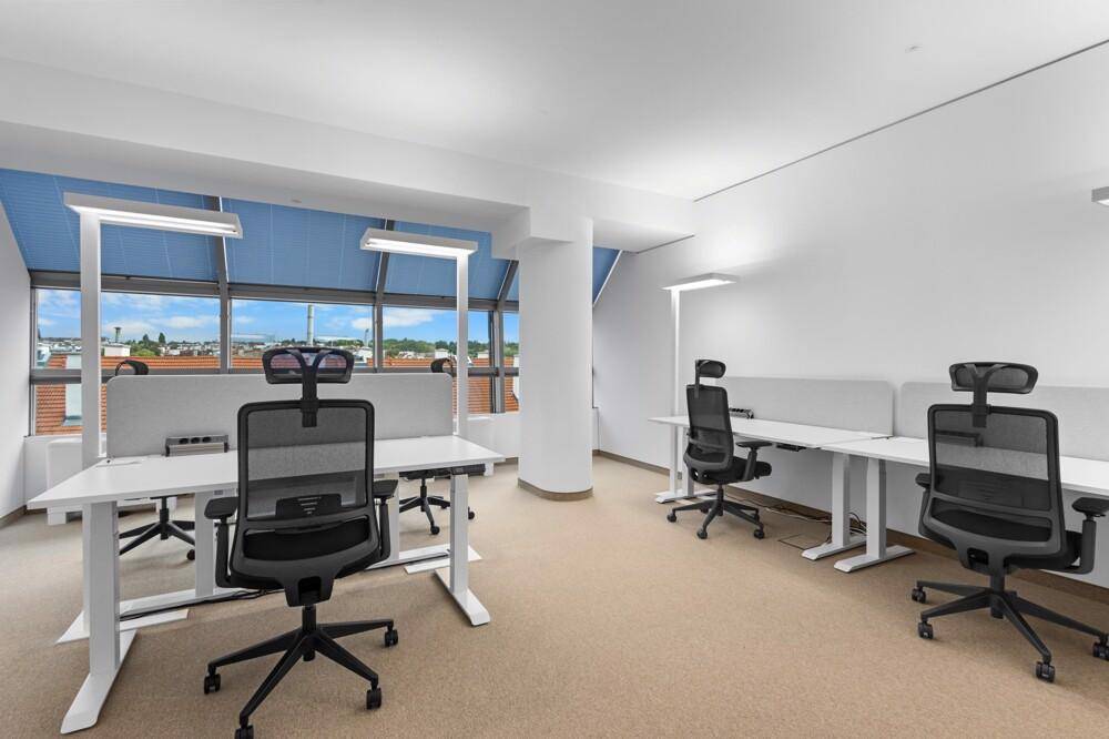 Offener Bürobereich im Obergeschoss mit vielen Fenstern, die einen weiten Blick über die Stadt bieten.
