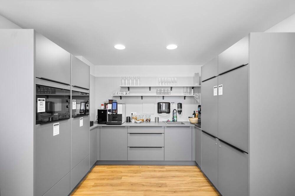 Moderne Teeküche mit grauen Schränken, Holzboden und integrierten Geräten für Mitarbeiter.