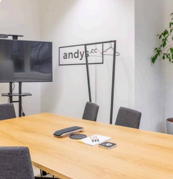 Heller Konferenzraum mit großem Bildschirm, Holztisch und minimalistischer Garderobe für professionelle Meetings.